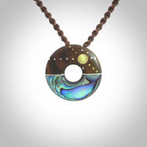 This photo shows a donut disc pendant hand carved from Lignum Vitae with premium nz paua shell, Mother of Pearl alongside; brass, copper and silver. This is a stand out one off necklace for those who appreciate art to wear. It is provided with a cord in brown that is a fixed length with Paua Shell Toggle. We ship this piece worldwide and shipping is included in the price.