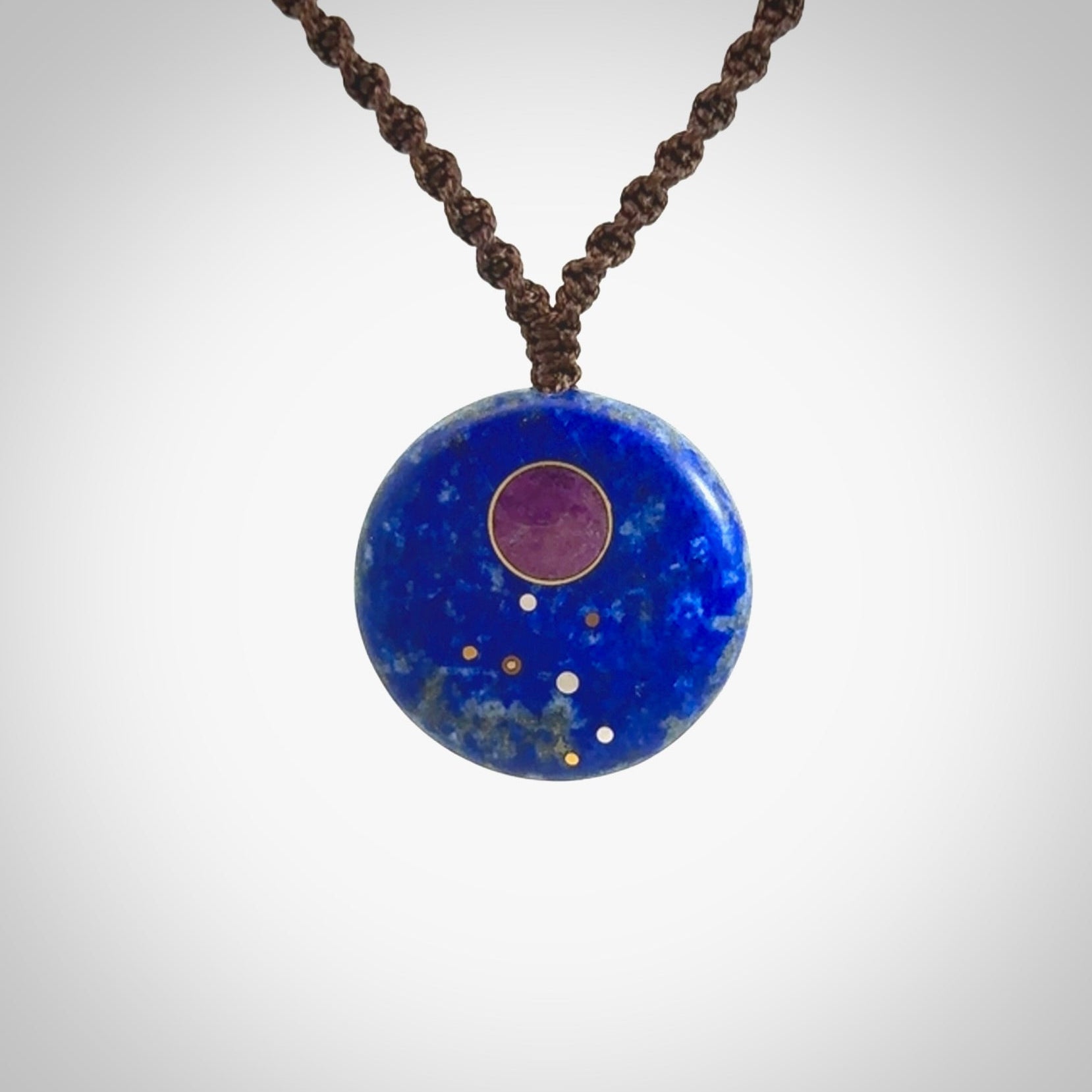 This photo shows a medium sized disc pendant hand carved from Lapis Lazuli with Sugilite inlay and copper, gold, and silver. This is a stand out one off necklace for those who appreciate art to wear. It is provided with a cord in black that is a fixed length with Paua Shell Toggle. We ship this piece worldwide and shipping is included in the price.