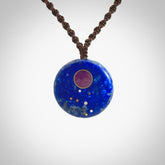 This photo shows a medium sized disc pendant hand carved from Lapis Lazuli with Sugilite inlay and copper, gold, and silver. This is a stand out one off necklace for those who appreciate art to wear. It is provided with a cord in black that is a fixed length with Paua Shell Toggle. We ship this piece worldwide and shipping is included in the price.
