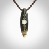 This photo shows a medium sized surfboard pendant hand carved from Lignum Vitae wood with Mother of Pearl and Paua Shell inlay, alongside; brass and silver. This is a stand out one off necklace for those who appreciate art to wear. It is provided with a cord in brown that is a fixed length with Paua Shell Toggle. We ship this piece worldwide and shipping is included in the price.