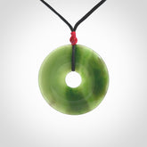 This picture shows a large hand-carved disc pendant. It is carved from British Columbian jade and is suspended from a hand-plaited, black cord. Free delivery worldwide. BC Jade contemporary necklace.