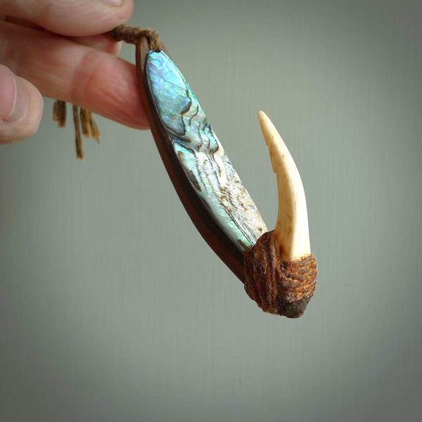 This picture shows a small sculptural hook called a pā kahawai. It is carved from whale bone, paua shell and wood, and is a colourful blue grey colour. It is shown on a stand made from argillite stone and is held in a brass cradle. One only, free shipping worldwide.