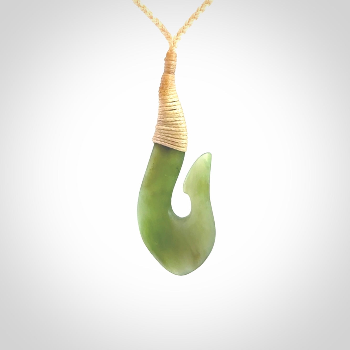 This picture shows a green jade hook pendant, also called a hei-matau, carved for us in New Zealand jade. The carver is Ric Moor - and this is a beautiful example of his work. The cord is a four-plait, adjustable fine beige coloured necklace.