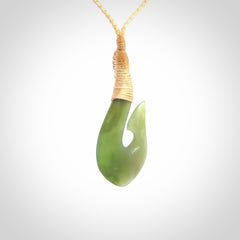 This picture shows a green jade hook pendant, also called a hei-matau, carved for us in New Zealand jade. The carver is Ric Moor - and this is a beautiful example of his work. The cord is a four-plait, adjustable fine beige coloured necklace.