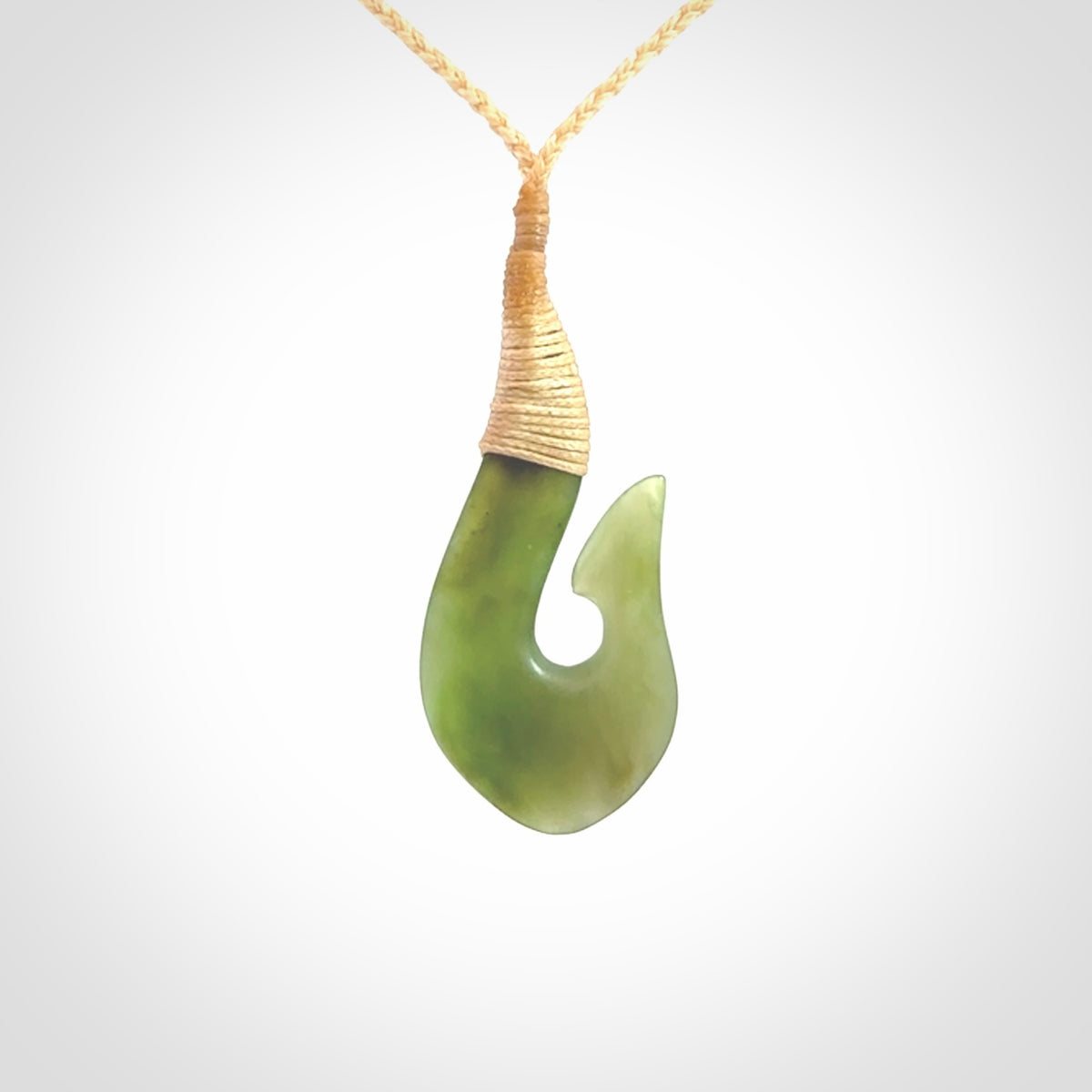 This picture shows a green jade hook pendant, also called a hei-matau, carved for us in New Zealand jade. The carver is Ric Moor - and this is a beautiful example of his work. The cord is a four-plait, adjustable fine beige coloured necklace.