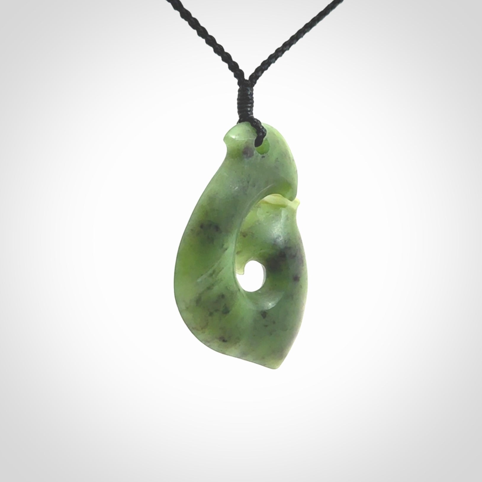 This picture shows a jade hook pendant, also called a hei-matau, carved for us in New Zealand jade. The cord is a four-plait, adjustable black coloured necklace.