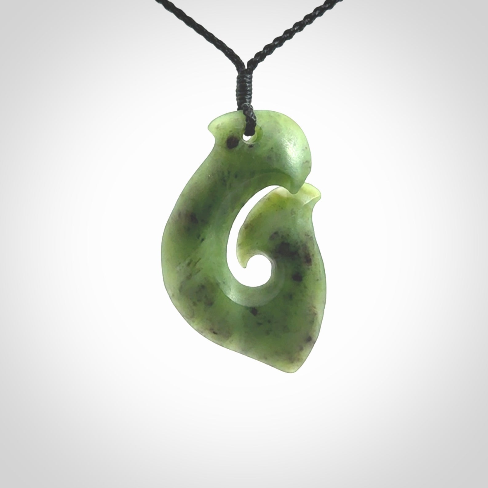 This picture shows a jade hook pendant, also called a hei-matau, carved for us in New Zealand jade. The cord is a four-plait, adjustable black coloured necklace.