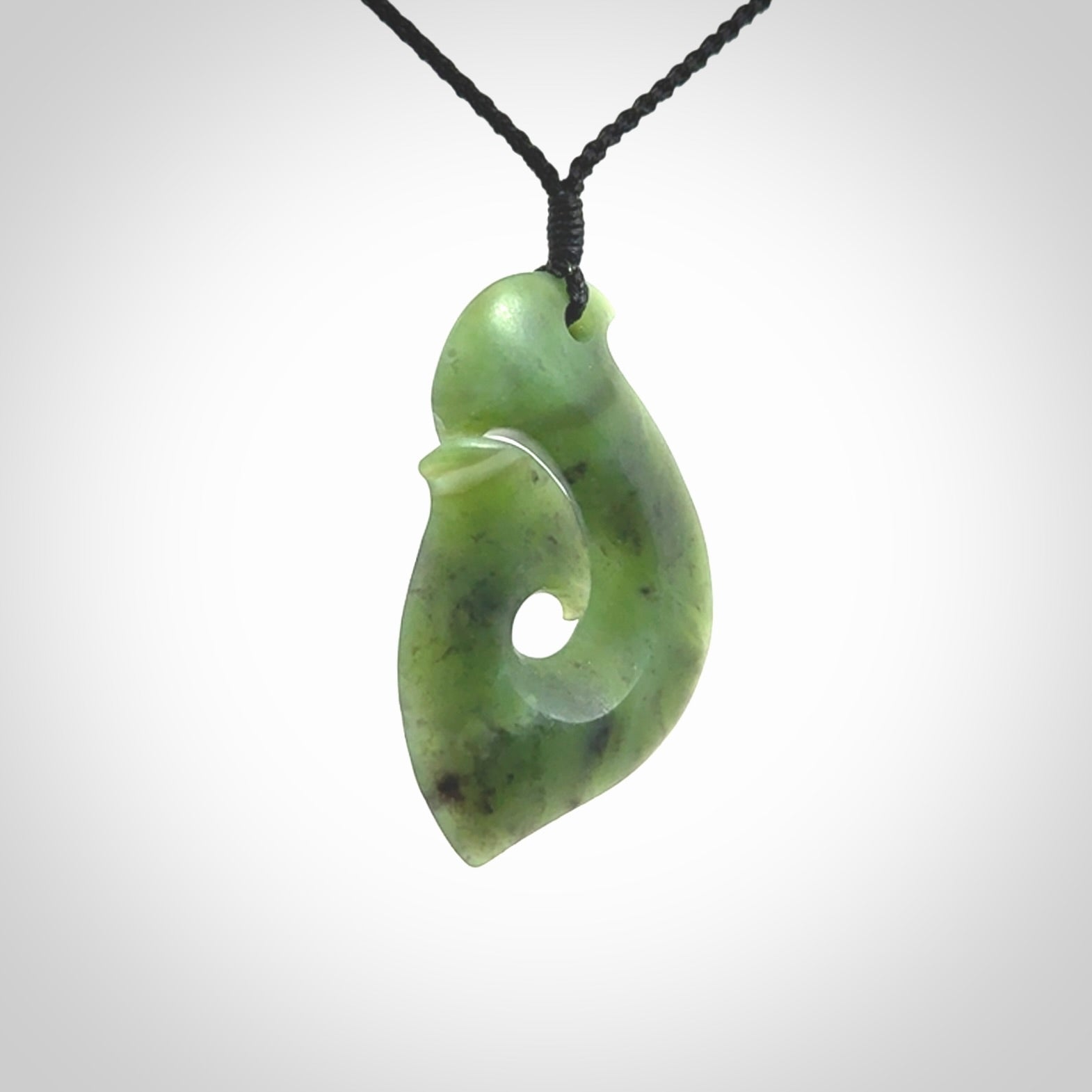 This picture shows a jade hook pendant, also called a hei-matau, carved for us in New Zealand jade. The cord is a four-plait, adjustable black coloured necklace.