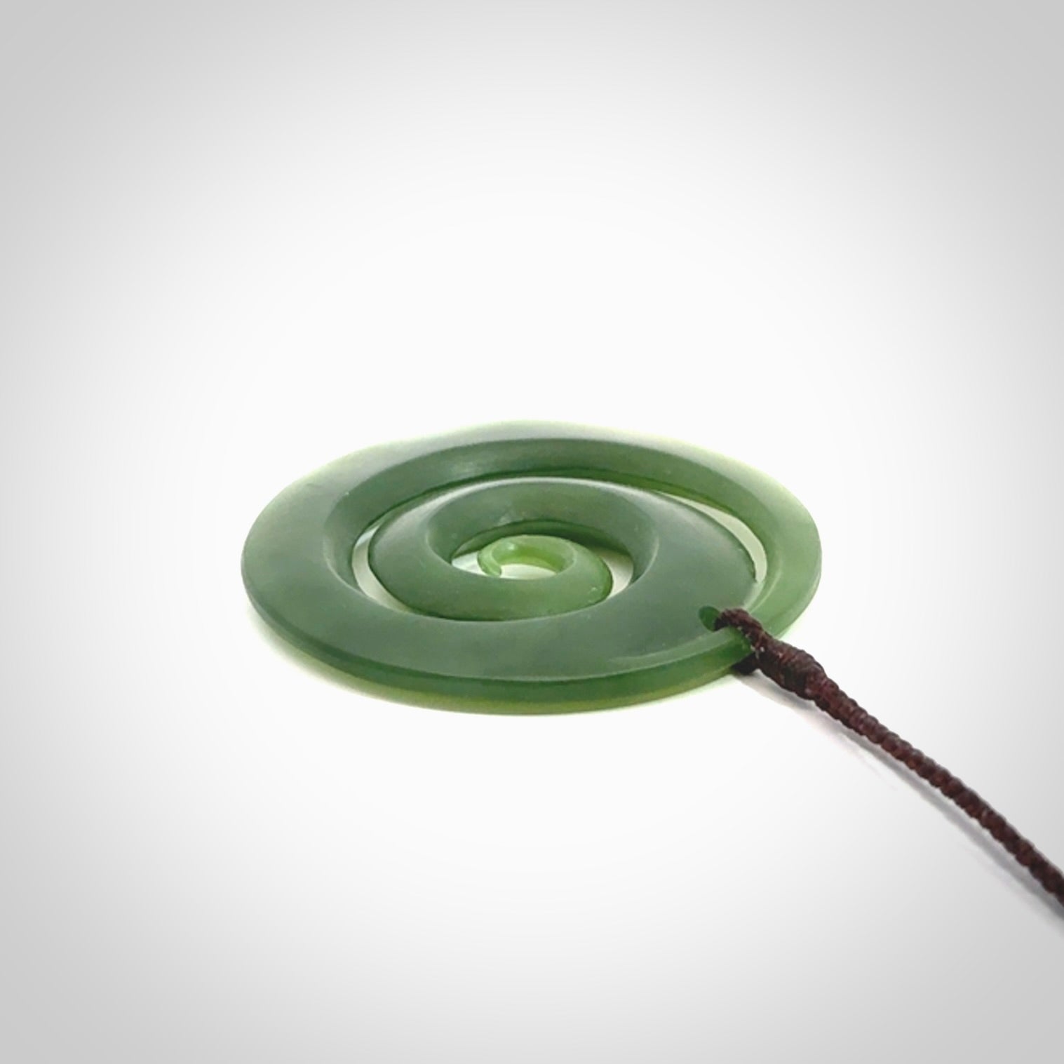 This picture shows a hand carved jade koru pendant. It is a darker green colour which is quite translucent where the jade is thin. The cord is hand plaited and adjustable so that you can position the pendant where it suits you best.