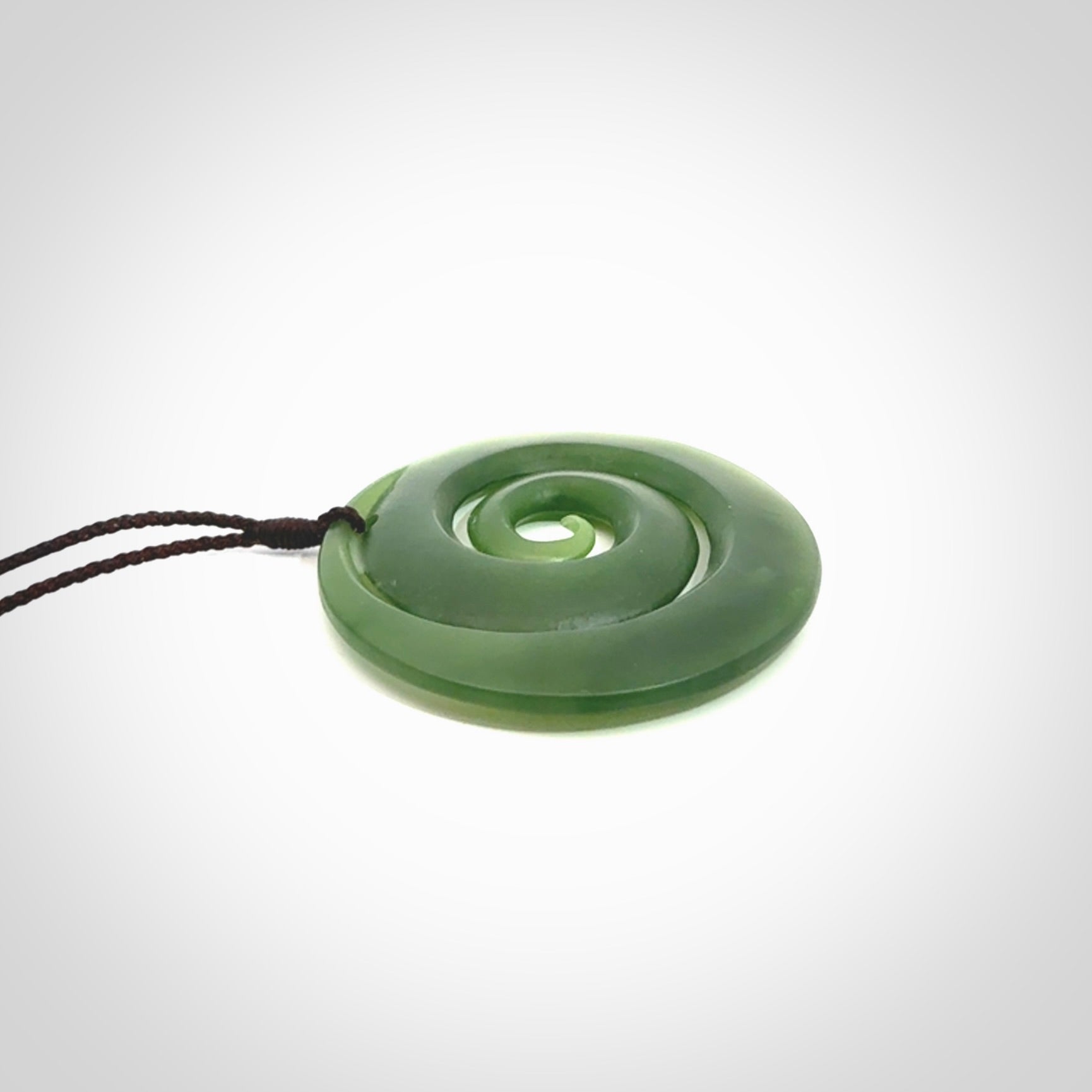 This picture shows a hand carved jade koru pendant. It is a darker green colour which is quite translucent where the jade is thin. The cord is hand plaited and adjustable so that you can position the pendant where it suits you best.