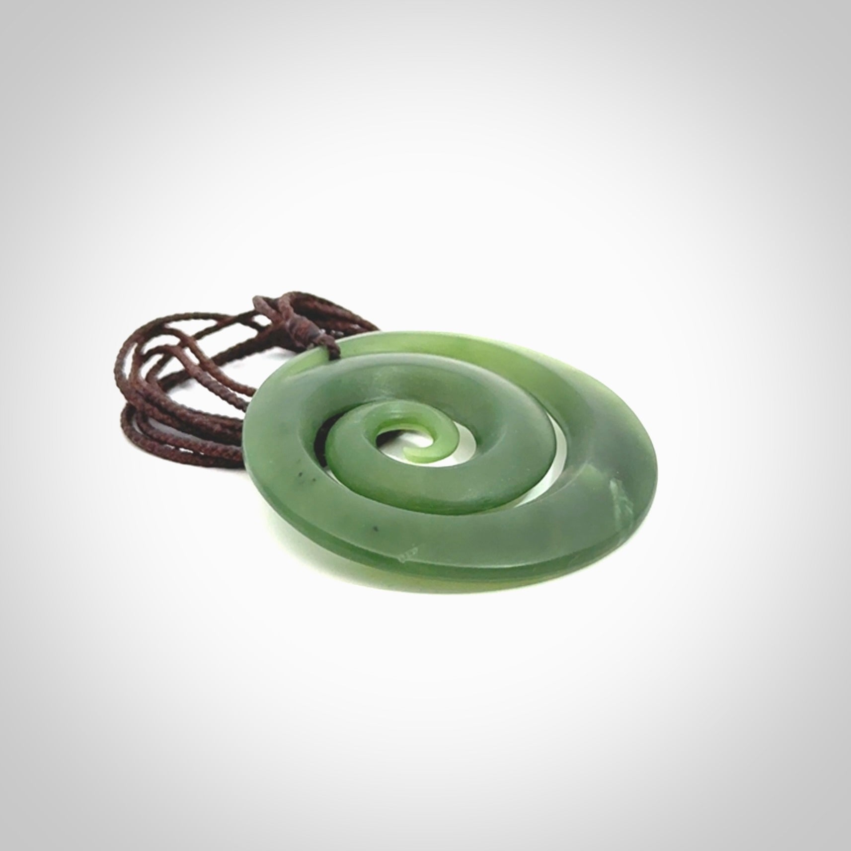 This picture shows a hand carved jade koru pendant. It is a darker green colour which is quite translucent where the jade is thin. The cord is hand plaited and adjustable so that you can position the pendant where it suits you best.