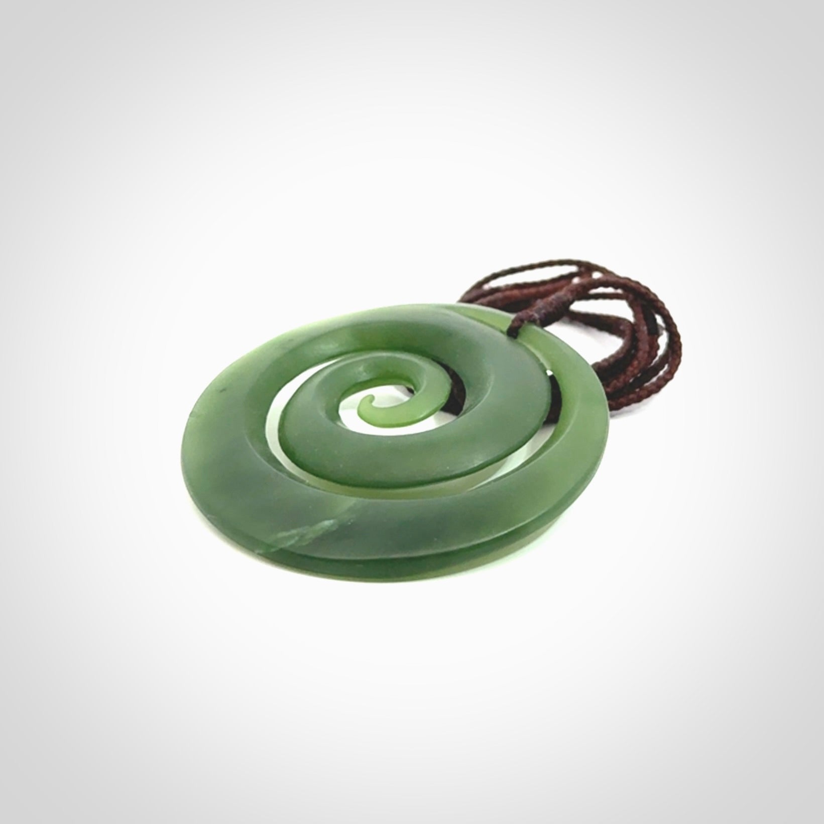 This picture shows a hand carved jade koru pendant. It is a darker green colour which is quite translucent where the jade is thin. The cord is hand plaited and adjustable so that you can position the pendant where it suits you best.