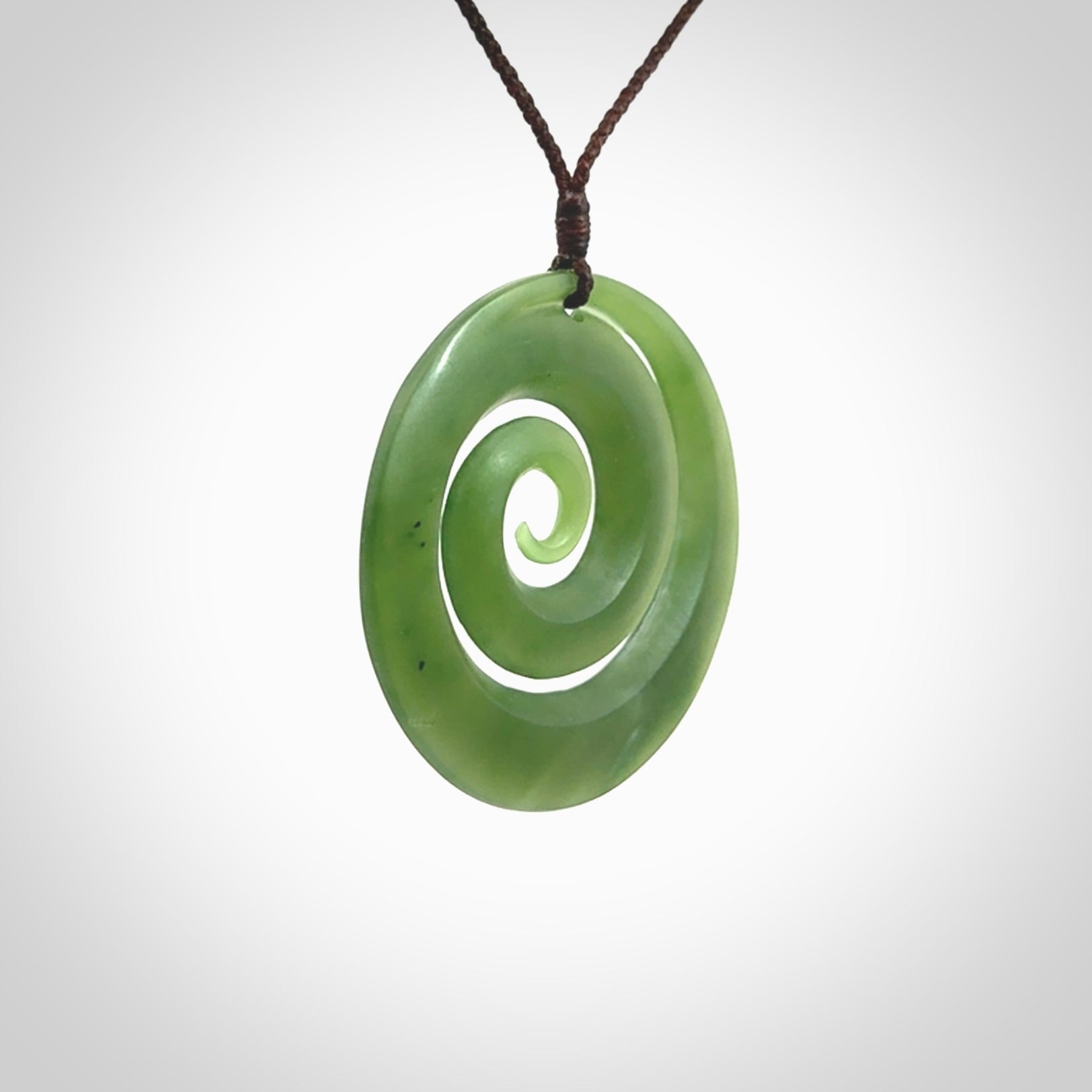 This picture shows a hand carved jade koru pendant. It is a darker green colour which is quite translucent where the jade is thin. The cord is hand plaited and adjustable so that you can position the pendant where it suits you best.