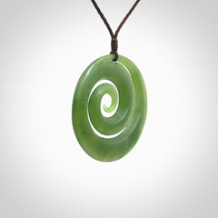 This picture shows a hand carved jade koru pendant. It is a darker green colour which is quite translucent where the jade is thin. The cord is hand plaited and adjustable so that you can position the pendant where it suits you best.