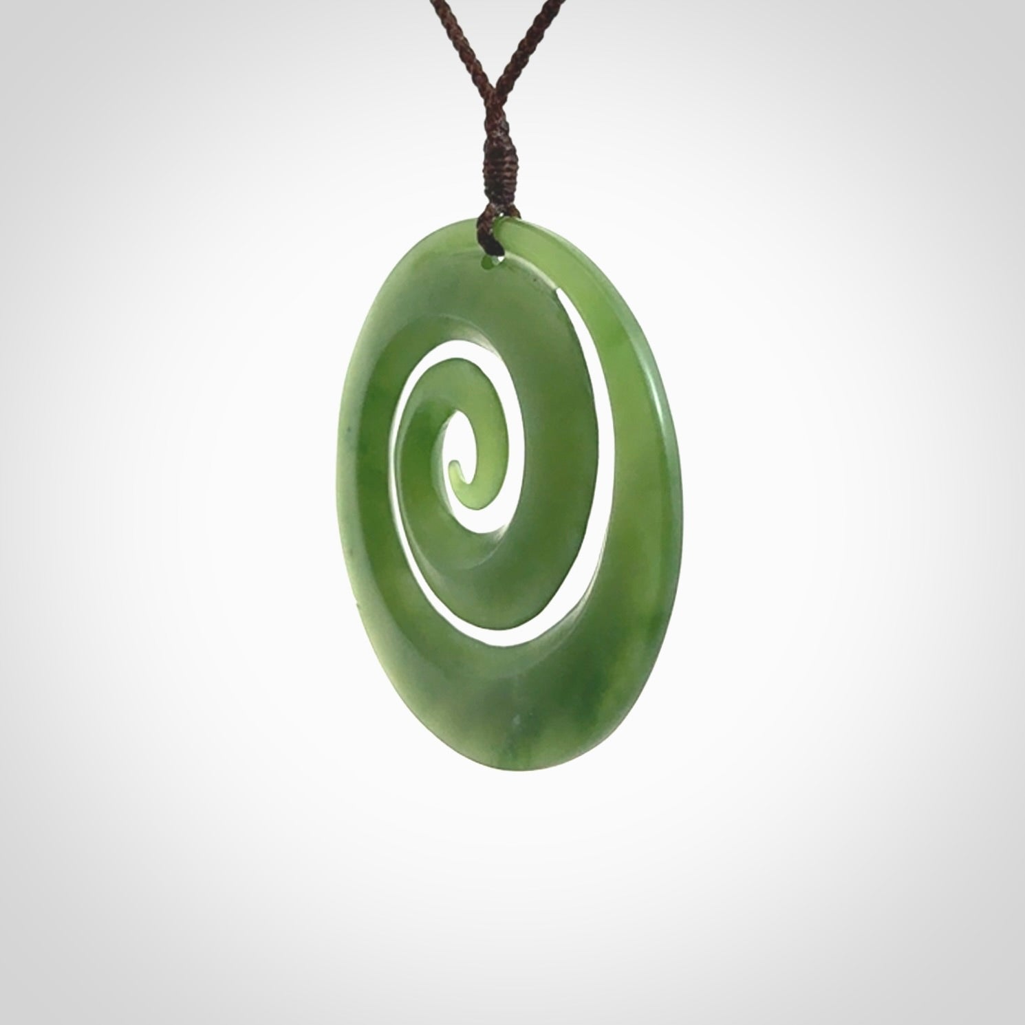 This picture shows a hand carved jade koru pendant. It is a darker green colour which is quite translucent where the jade is thin. The cord is hand plaited and adjustable so that you can position the pendant where it suits you best.