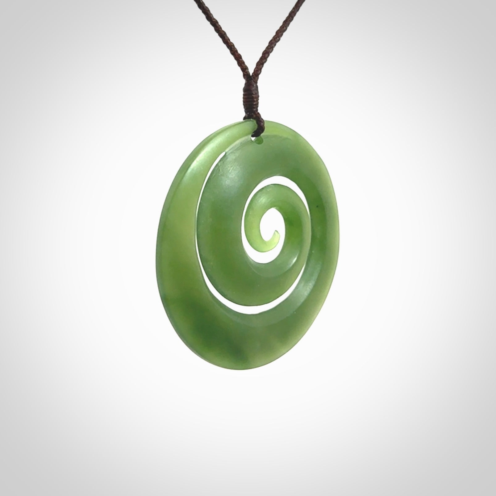 This picture shows a hand carved jade koru pendant. It is a darker green colour which is quite translucent where the jade is thin. The cord is hand plaited and adjustable so that you can position the pendant where it suits you best.