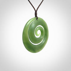 This picture shows a hand carved jade koru pendant. It is a darker green colour which is quite translucent where the jade is thin. The cord is hand plaited and adjustable so that you can position the pendant where it suits you best.