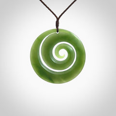 This picture shows a hand carved jade koru pendant. It is a darker green colour which is quite translucent where the jade is thin. The cord is hand plaited and adjustable so that you can position the pendant where it suits you best.
