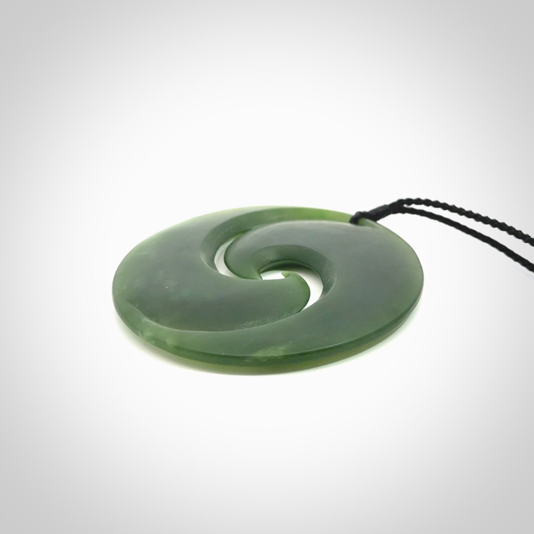 This picture shows a large hand carved jade koru pendant. It is a darker green colour which is quite translucent where the jade is thin. Although a large piece, it is a wonderful, delicate piece of jewellery. The cord is hand plaited and adjustable so that you can position the pendant where it suits you best.