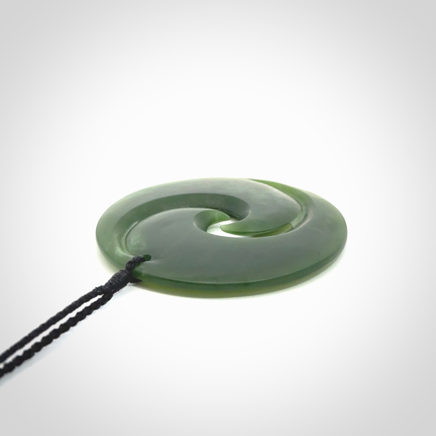 This picture shows a large hand carved jade koru pendant. It is a darker green colour which is quite translucent where the jade is thin. Although a large piece, it is a wonderful, delicate piece of jewellery. The cord is hand plaited and adjustable so that you can position the pendant where it suits you best.