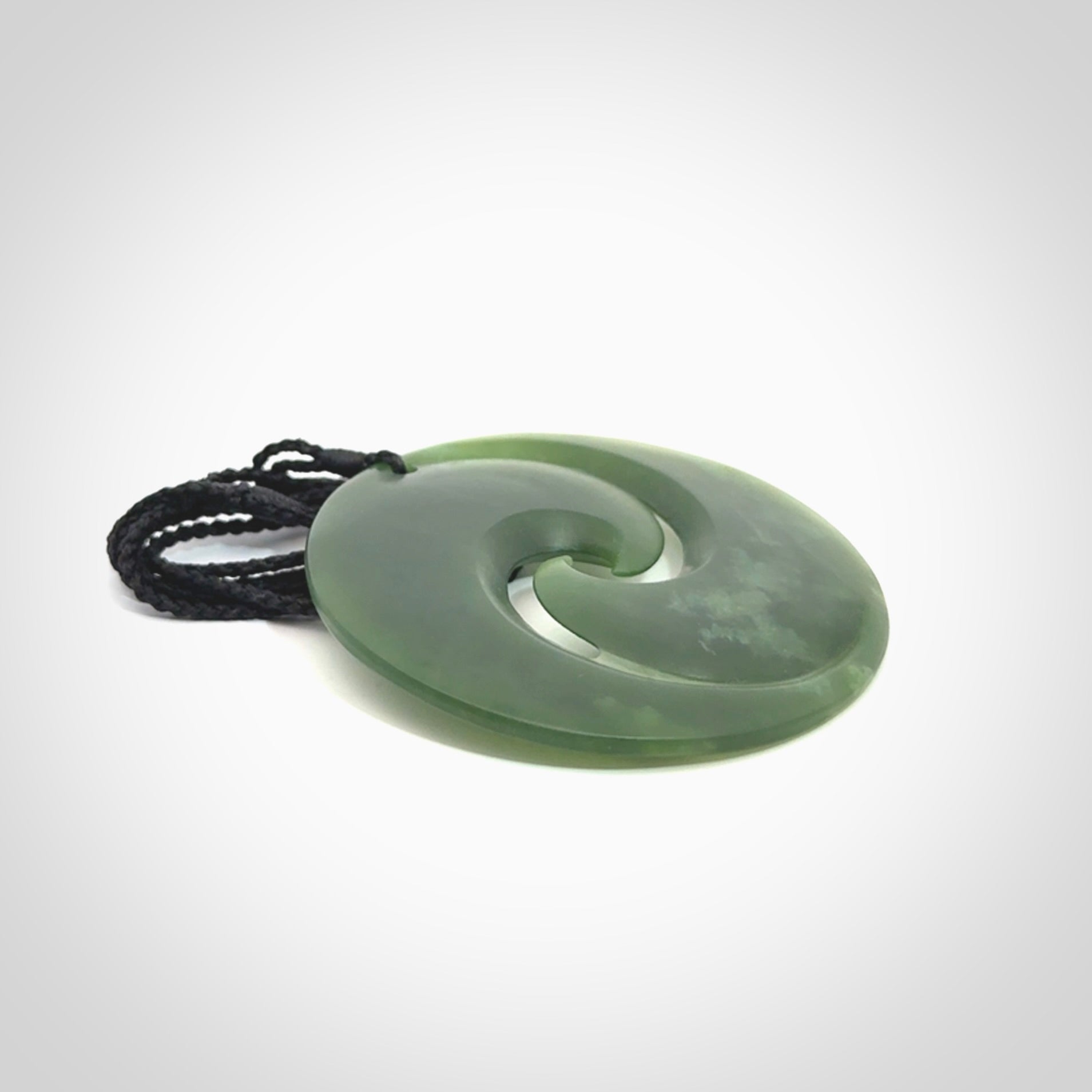 This picture shows a large hand carved jade koru pendant. It is a darker green colour which is quite translucent where the jade is thin. Although a large piece, it is a wonderful, delicate piece of jewellery. The cord is hand plaited and adjustable so that you can position the pendant where it suits you best.