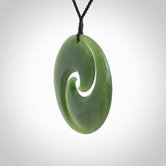This picture shows a large hand carved jade koru pendant. It is a darker green colour which is quite translucent where the jade is thin. Although a large piece, it is a wonderful, delicate piece of jewellery. The cord is hand plaited and adjustable so that you can position the pendant where it suits you best.