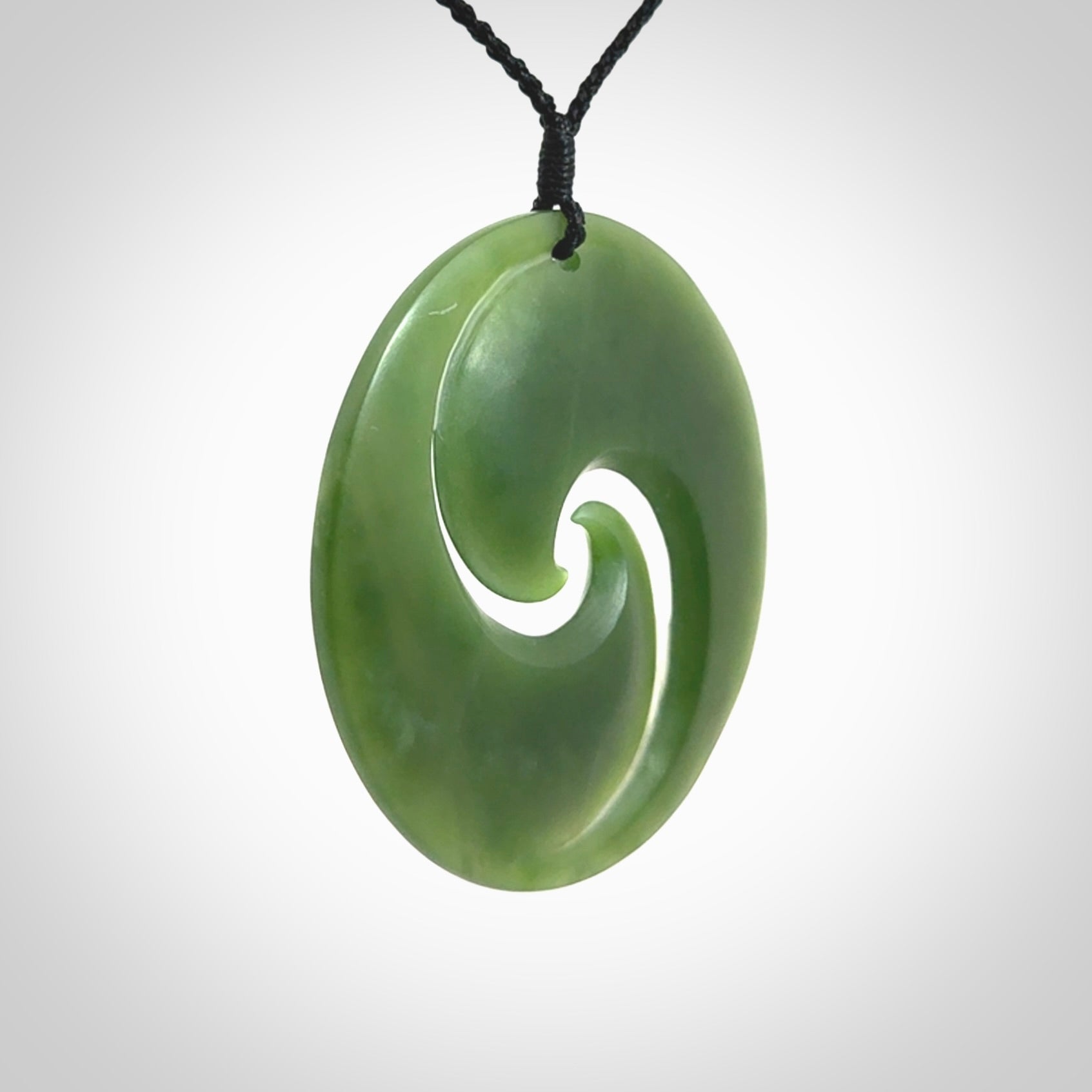 This picture shows a large hand carved jade koru pendant. It is a darker green colour which is quite translucent where the jade is thin. Although a large piece, it is a wonderful, delicate piece of jewellery. The cord is hand plaited and adjustable so that you can position the pendant where it suits you best.