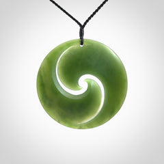 This picture shows a large hand carved jade koru pendant. It is a darker green colour which is quite translucent where the jade is thin. Although a large piece, it is a wonderful, delicate piece of jewellery. The cord is hand plaited and adjustable so that you can position the pendant where it suits you best.