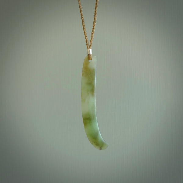 This picture shows a hand carved Spoon River White Jade drop pendant with adjustable cord. The jade is a very light, white green with a shimmer of darker tones in the stone. It is suspended from a tan coloured cord. Delivery is free worldwide.