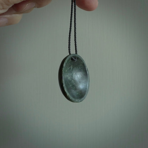 This piece is a oval round, disc pendant. It was carved for us by Ric Moor from a lovely light and milky green piece of New Zealand jade. It is suspended on a black coloured braided cord that is length adjustable.