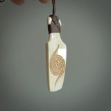 Hand carved engraved bone toki necklace hand made here in New Zealand. One only artistic toki pendant with hand plaited dark brown adjustable cord. Shipped to you with Express Courier. Stand out toki pendant for men and women. Bone Toki with engraved spiral on the back and paua shell insert on the front.
