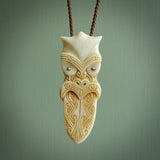 This is a large carved Koruru pendant. It is made from two materials - New Zealand Paua Shell and Bone. The face of the Koruru is carved with a traditional design in the front. It has a protruding tongue which is also carved and the back face has traditional carved designs. This is a large and very traditional pendant that is a collectors piece. This piece is provided on a brown adjustable cord.