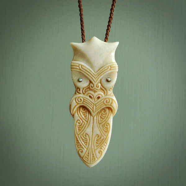 This is a large carved Koruru pendant. It is made from two materials - New Zealand Paua Shell and Bone. The face of the Koruru is carved with a traditional design in the front. It has a protruding tongue which is also carved and the back face has traditional carved designs. This is a large and very traditional pendant that is a collectors piece. This piece is provided on a brown adjustable cord.