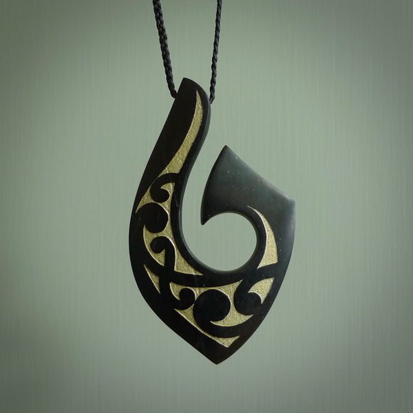 A hand carved hook design pendant, carved in New Zealand Tangiwai Jade with Gold Enamel. The colour is a beautiful dark and deep green and it is engraved on one side with a flowing design. The cord is black and is length adjustable.