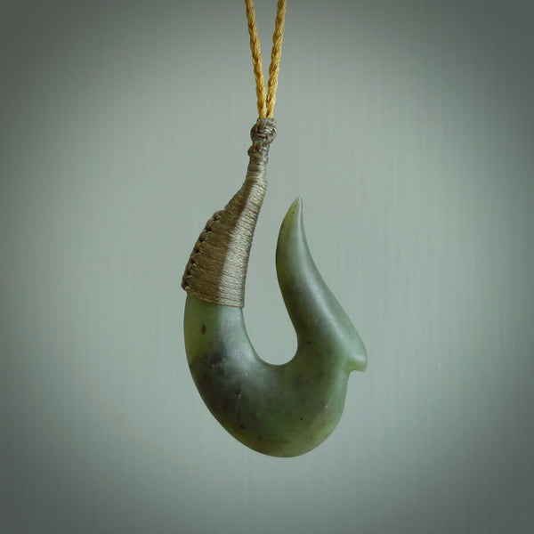 This photo shows a greenstone hook, or matau, pendant. It is a beautiful green kahurangi jade. The cord is plaited and the length can be adjusted.