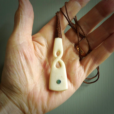 This picture shows a carved twist in bone. It is a twist shaped pendant. Hand made by Andrew Doughty. It is provided with a hand-plaited brown cord that is length adjustable. Shipping is included and we ship worldwide.
