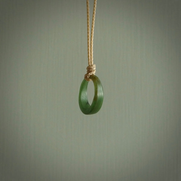 This piece is a oval round, ring pendant. It was carved for us by Ric Moor from a lovely light and milky green piece of New Zealand jade. It is suspended on a beige coloured braided cord that is length adjustable.