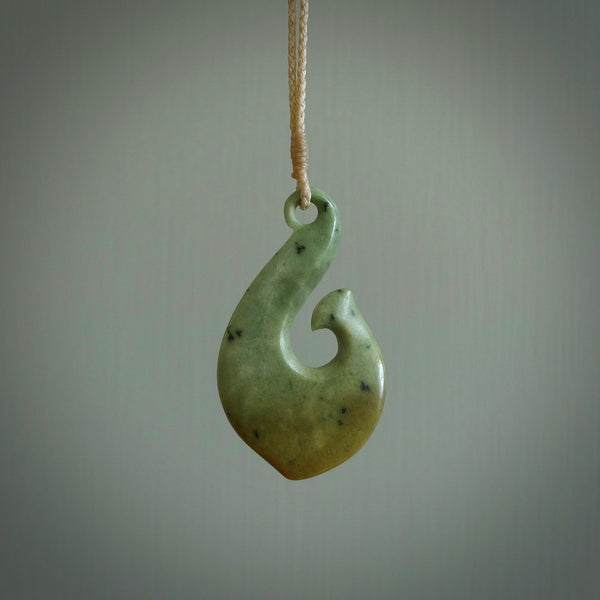 This picture shows a jade hook pendant, also called a hei-matau, carved for us in New Zealand jade. The jade is a wonderful deep mint green pounamu. This is a rare jade loved and valued for its distinctive colour. The carver is Ric Moor - and this is a beautiful example of his work. The cord is a four-plait, adjustable brown coloured necklace.