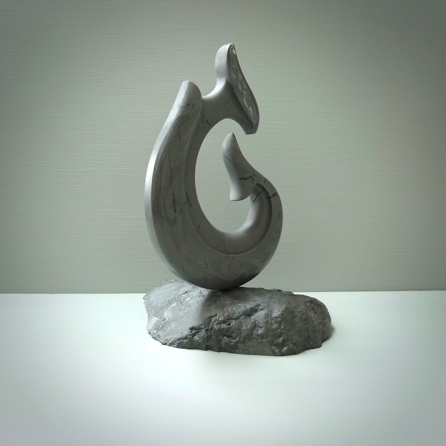 Hand carved large New Zealand Argillite Stone Matau, hook carving displayed in a New Zealand Pākohe stand sculpture. Hand carved here in New Zealand by Kerry Thompson. This is a 'one only' sculpture, a beautiful display piece.