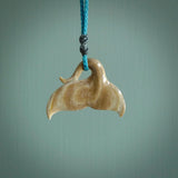 This picture shows a hand carved whale tail pendant. It is a dark, ginger brown colour and is handcarved from Woolly Mammoth tusk. The necklace is made from a braided cord in a paradise blue colour.