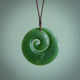 This picture shows a large hand carved jade koru pendant. It is a darker green colour which is quite translucent where the jade is thin. Although a large piece, it is a wonderful, delicate piece of jewellery. The cord is hand plaited and adjustable so that you can position the pendant where it suits you best. This koru was carved for us by Ric Moor. Delivery is free worldwide.