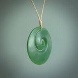 This picture shows a hand carved jade koru pendant. It is a deep green with orange colour and is a wonderful, large sized piece of jewellery. The cord is a four plait beige colour and adjustable so that you can position the pendant where it suits you best. This koru was carved for us by Ric Moor. Delivery is free worldwide.