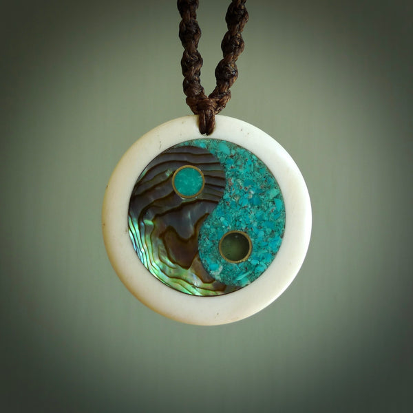 This photo shows a medium sized yin and yang pendant hand carved from bone with Mother of Pearl, Lapis Lazuli and Paua Shell inlay and brass. This is a stand out one off necklace for those who appreciate art to wear. It is provided with a cord in black that is a fixed length with Paua Shell Toggle. We ship this piece worldwide and shipping is included in the price.