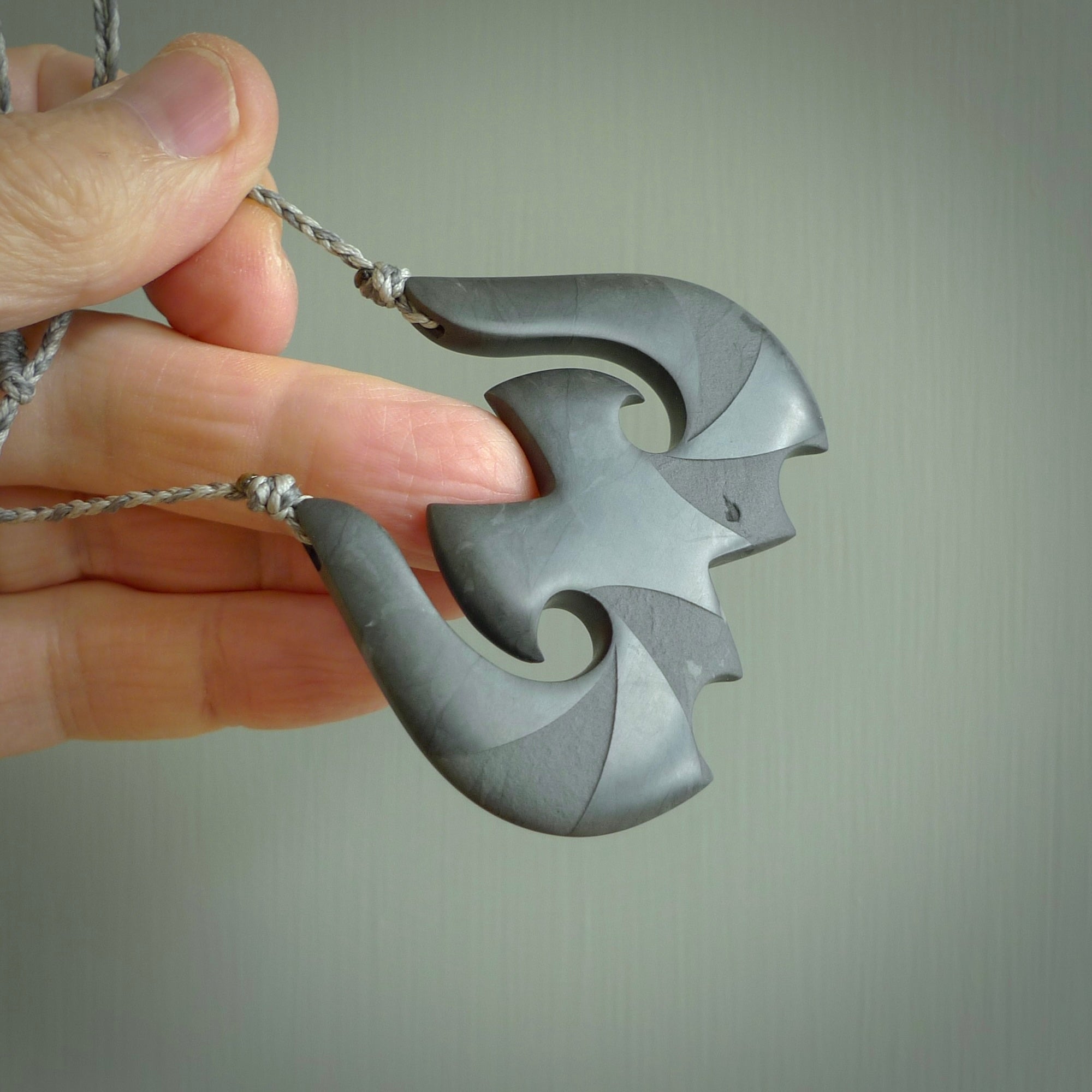 A hand carved large New Zealand Argillite double Hook, Matau, necklace. The cord is a black colour and is adjustable in length. A large sized hand made double hook necklace by New Zealand artist Rueben Tipene. One off work of art to wear.