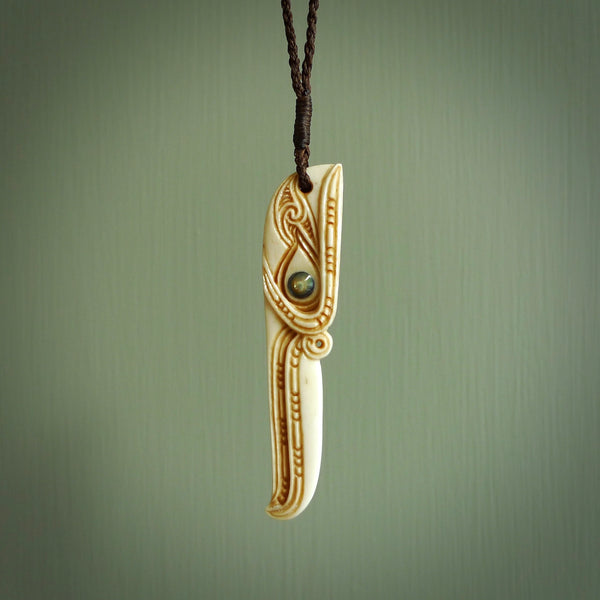 This picture shows a carved kāhu, hawk in bone. It is a drop shaped pendant. The artist has carved traditional decorative kowhaiwhai designs into the body and these run up the sides of the hawk. These have specific meanings. It is provided with a hand-plaited brown cord that is length adjustable. Shipping is included and we ship worldwide.