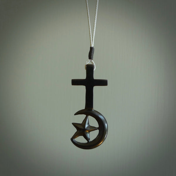 This pendant is a series of religious symbols carved in one piece of black jade. The top is a christian cross and at the bottom is the crescent of islam. It is suspended on a snowstorm grey plaited cord which is length adjustable.