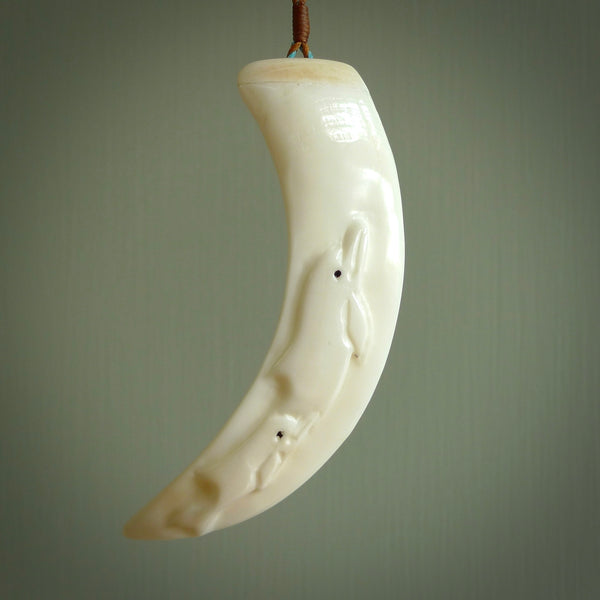 Hand carved dolphin pendant, carved by us. This piece is carved from boars tusk and is a fantastic depiction of these playful water mammals. This particular piece is a pair of dolphins swimming one behind the other. They are lovingly carved into the side of the tusk. The tusk is suspended from a bright red neck cord which is length adjustable.