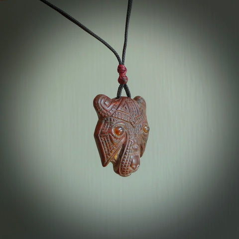 This picture shows a tiger pendant that we designed in jasper stone with amber inlay eyes. It is a tiger head that is carved in detail. A really attractive and eye-catching piece of handmade jewellery. The cord is hand plaited braid in black and the length can be adjusted.