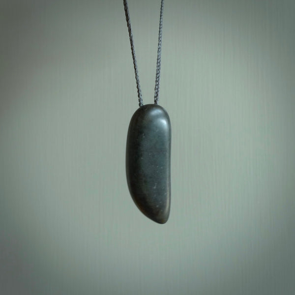 Greywacke Beach Stone drop, pendant hand made here in New Zealand. Hand carved by Rhys Hall for NZ Pacific. Handmade jewellery for sale online. The cord is grey and has a loop and pebble toggle closure. Unique necklace for men and women. Drop necklace hand made from New Zealand Greywacke Beach Stone.