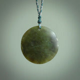 Hand carved jade disc pendant. One side has a double koru etched into the face. This is a subtle and beautiful design. The other side is plain. The cord is a tan colour and is adjustable. The piece was carved for NZ Pacific by Rueben Tipene.